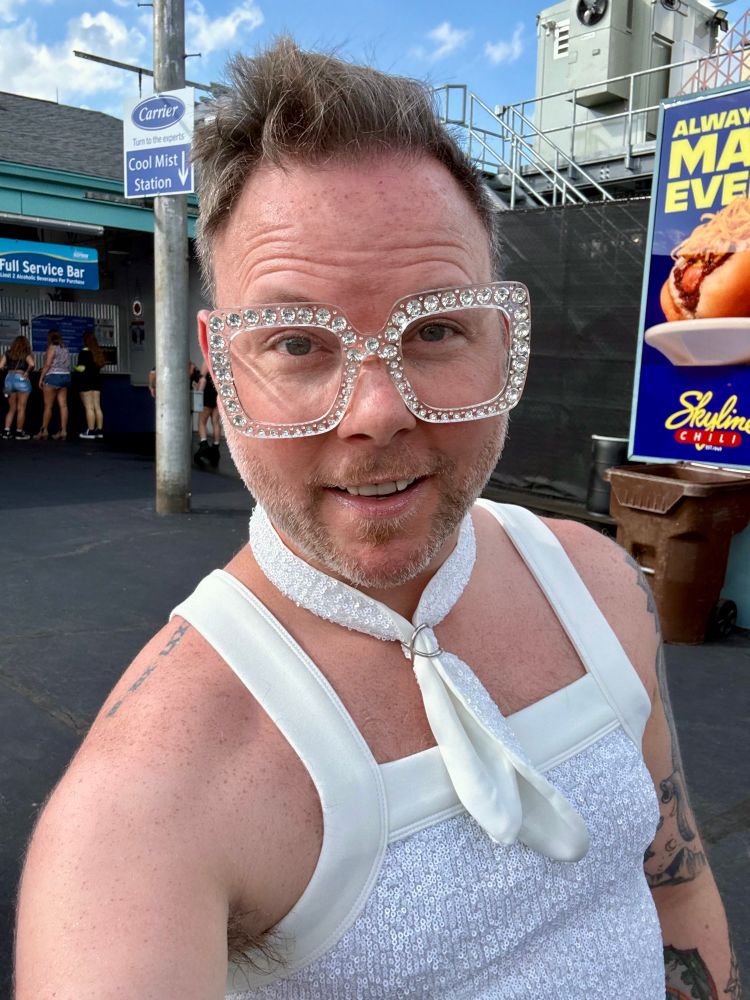 KP wearing a white sequin tank top, white sequin scarf, and clear glasses with rhinestones. 