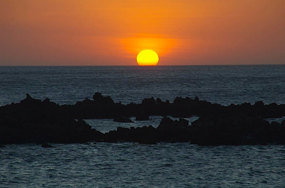 The sun sets over the ocean, with lava rock outcroppings in the foreground. Taken on the Kohala Coast, Hawaii.