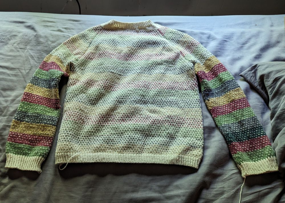 A hand knit sweater on a bed.