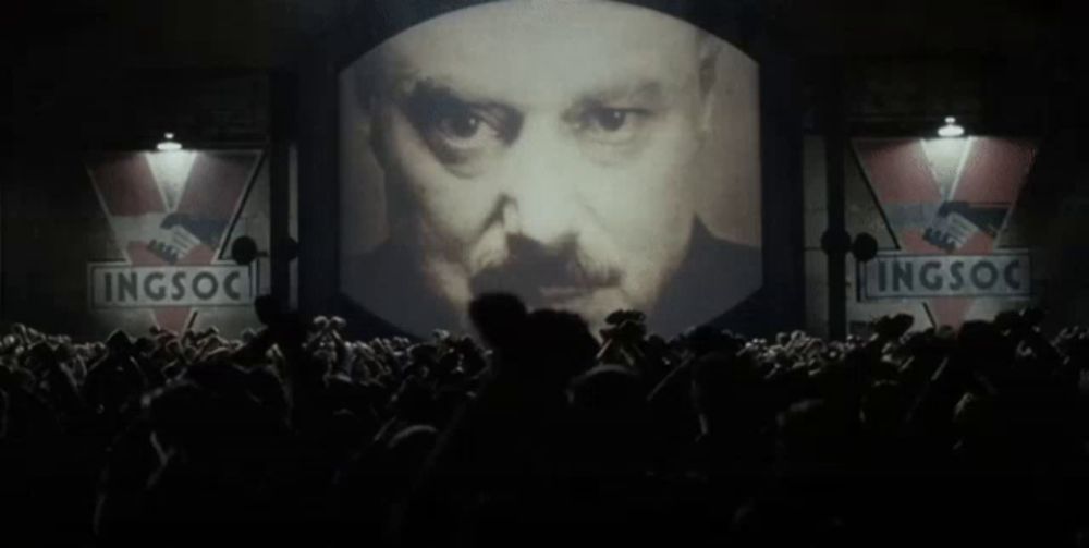 a large screen shows a man 's face and says ingsoc