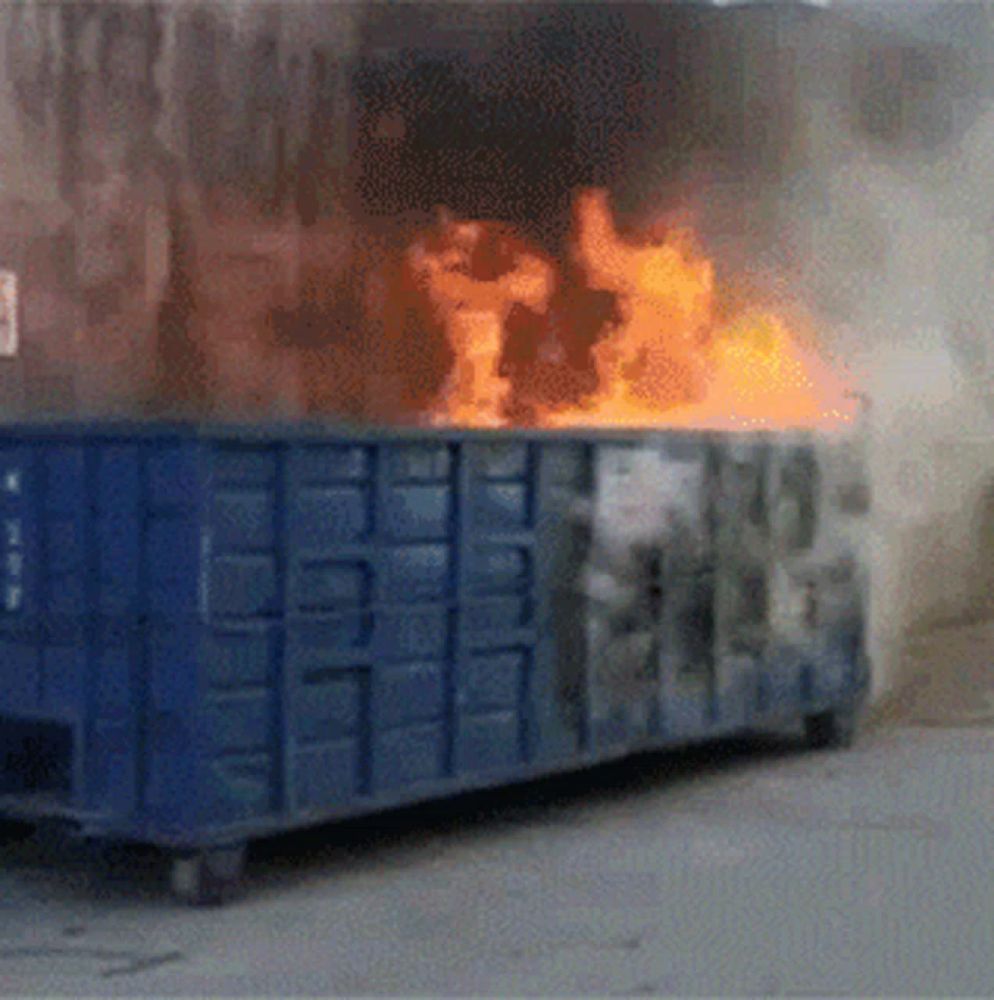 a blue dumpster is on fire and smoke is coming out of it with a sign on the side that says " no smoking "