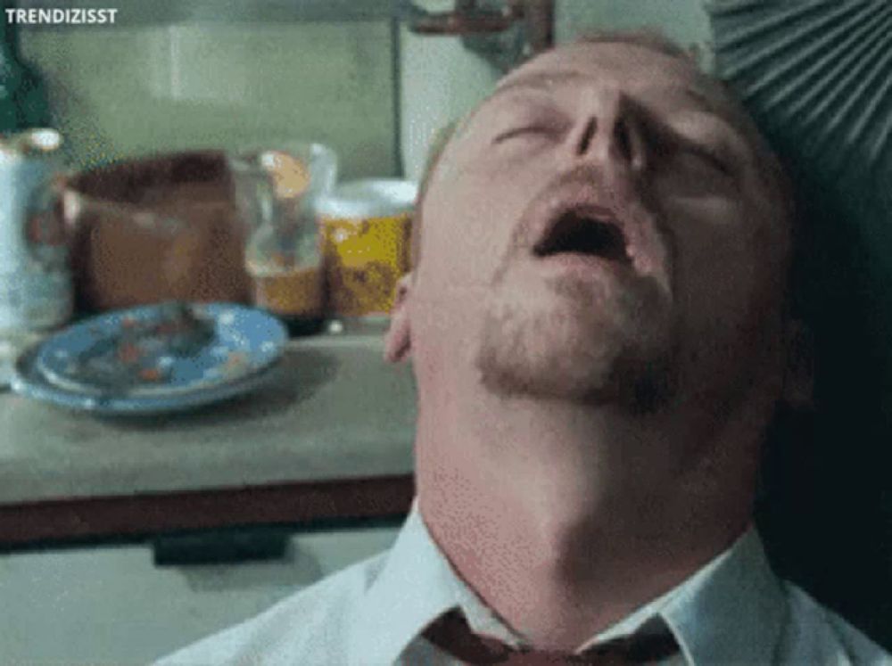 a man in a tie is yawning in a kitchen with a plate of food in the background