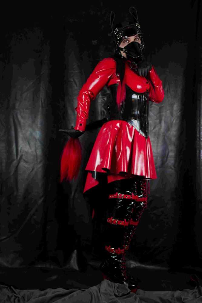 Pixel in a red and black latex outfit in front of a latex backdrop 