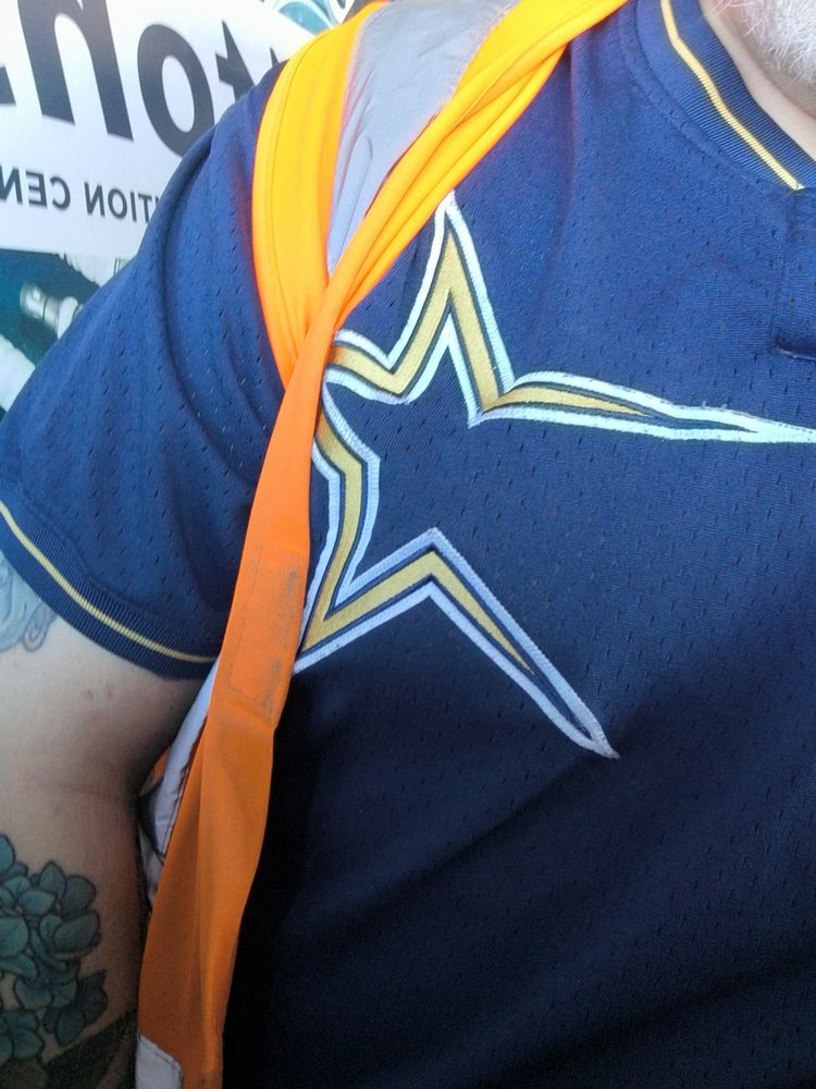 Half of a blue retro Astros batting practice jersey under a high visibility vest