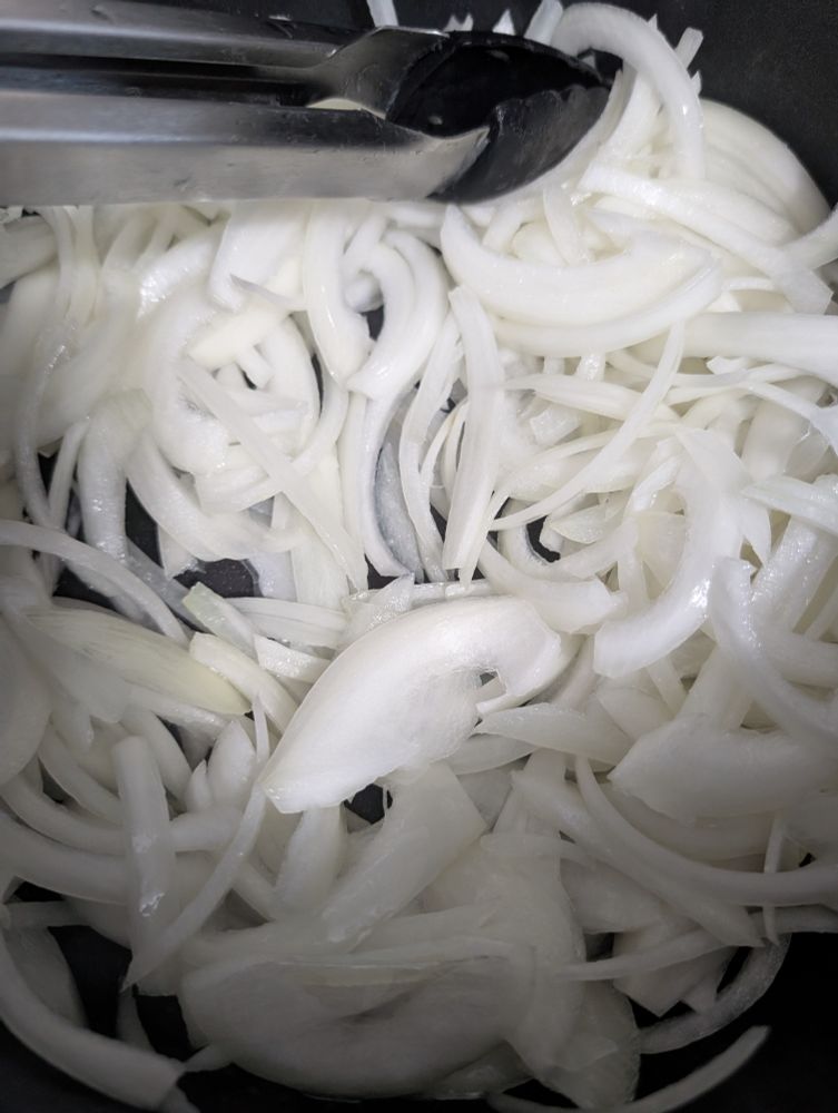 Sliced up onions in the bottom of a black pot 