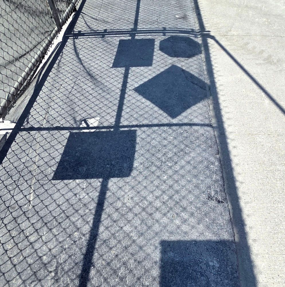 Shadow of a metal gate on the sidewalk at a construction site with geometric shapes of the shadows of the various signs. 