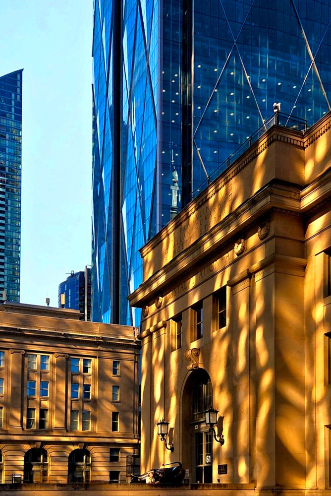 Morning sun reflecting off unseen glass skyscraper onto 20th century Beaux-Arts-style Union Station in downtown Toronto. Shadows are created by the steel between the panes of glass. Modern blue glass and steel skyscrapers rise behind, with a strip of pale blue sky between. 