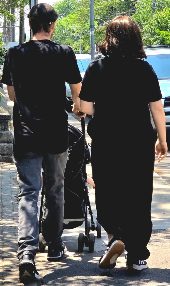 A couple wearing black and pushing a black stroller down the sidewalk. 