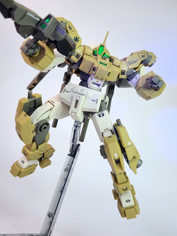 A close up photo of a completed HG Demi Barding model kit from Mobile Suit Gundam: The Witch from Mercury. The kit is facing the camera and is in a shooting pose on an action base with its rifle in its right hand and the head camera is illuminated with a black light.
