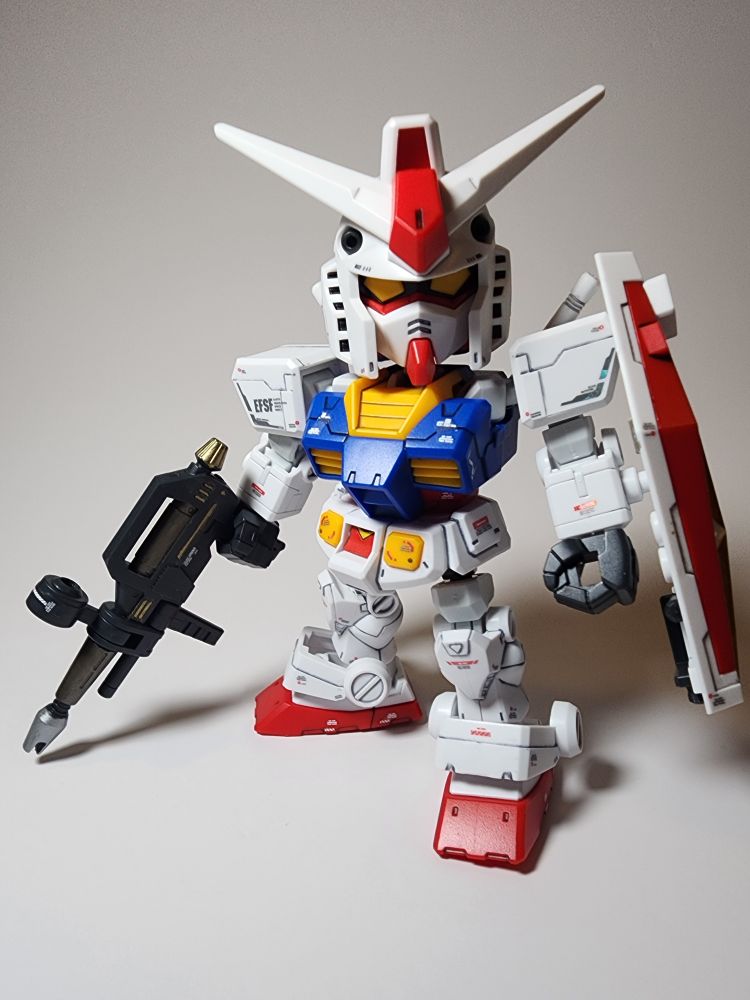 A SDCS model kit of the RX-78-2 Gundam from Mobile Suit Gundam. The kit has waterslide decals applied and is posed facing the camera. In its right hand it is holding its beam rifle and in its left it is holding its shield. 