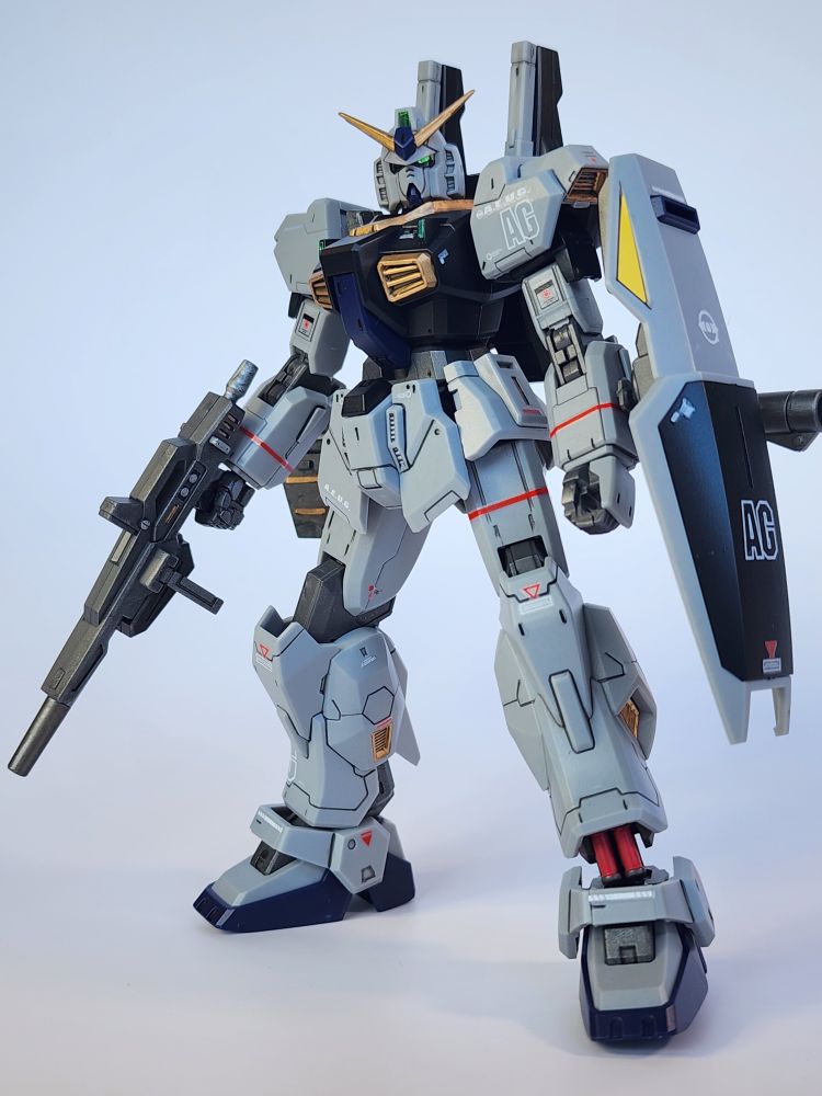 A completed model kit of the HG Gundam Mk-II AEUG 21st Century Real Type Version from JMS. The kit is standing holding its rifle in its right hand and is facing the camera.