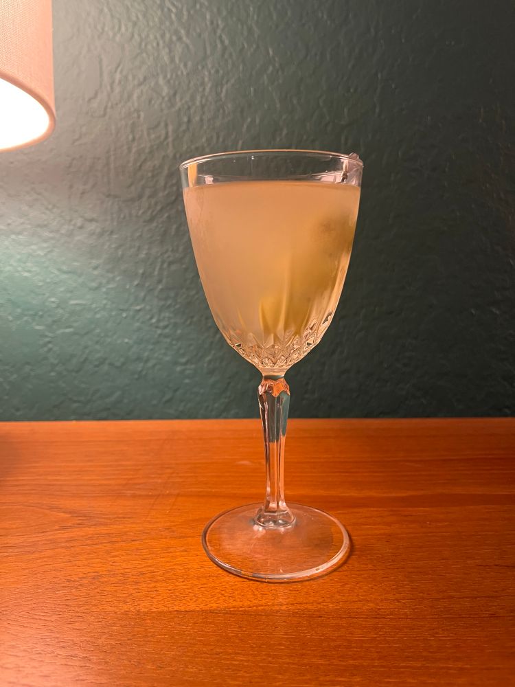 Cloudy dirty martini in a nick and nora with a skewer of olives
