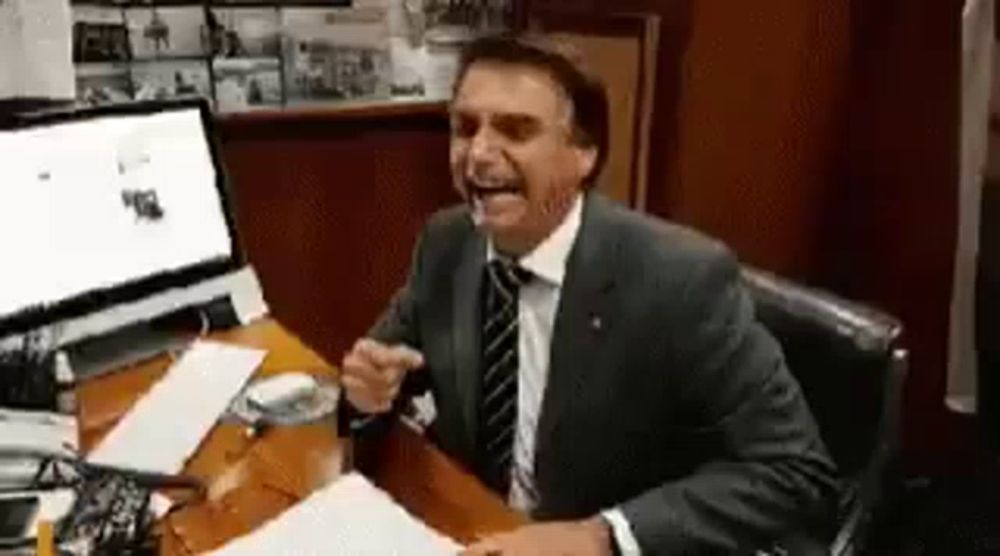 a man in a suit and tie is sitting at a desk laughing .