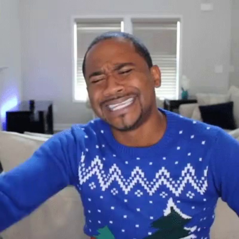 a man wearing a blue christmas sweater is sitting on a couch .