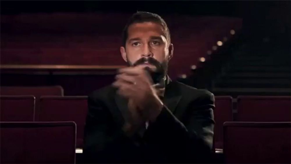 a man in a tuxedo and bow tie is clapping his hands in an auditorium .