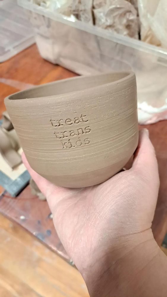 Unfired ceramic vessel with "treat trans kids" stamped on the side