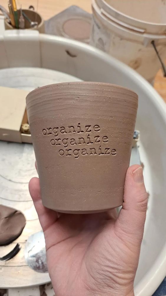 Unfired ceramic vessel with "organize organize organize"stamped on the side