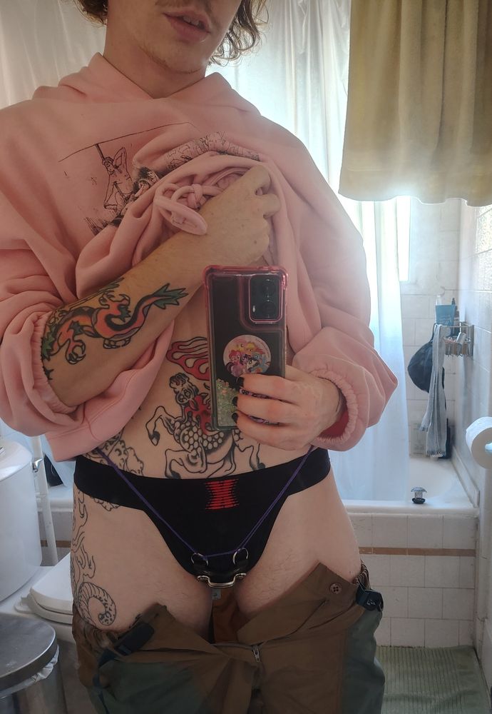 The poster reveals his cage and jockstrap beneath the shorts, pulling up the hoodie to reveal his stomach