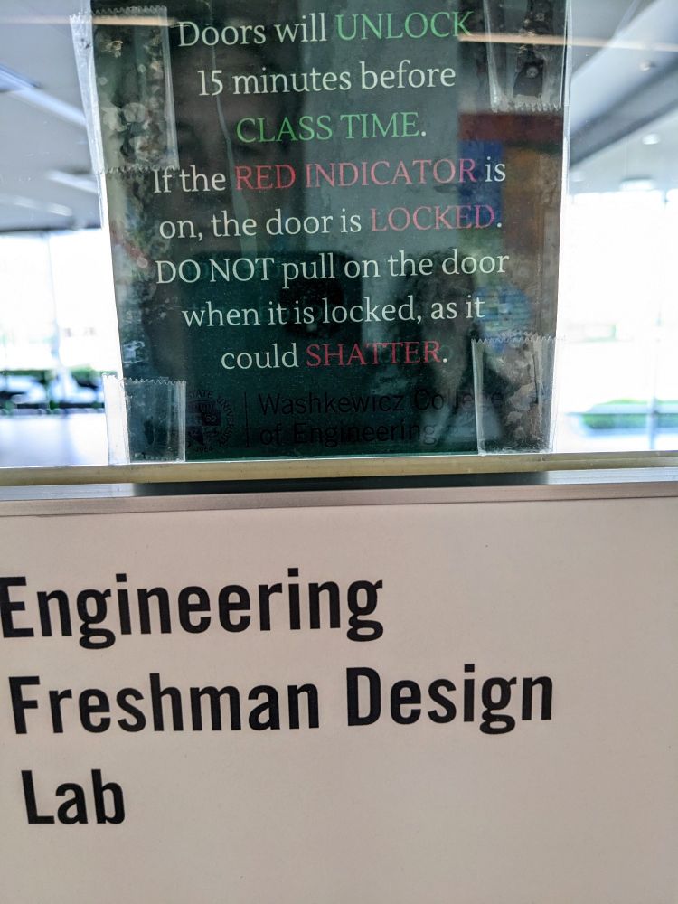 Sign on glass wall reading: Engineering Freshman Design Lab.
Above the sign is a paper taped onto the glass that states: "Doors will UNLOCK 15 minutes before CLASS TIME. If the RED INDICATOR is on, the door is LOCKED. DO NOT pull on the door when it is locked, as it could SHATTER the glass."