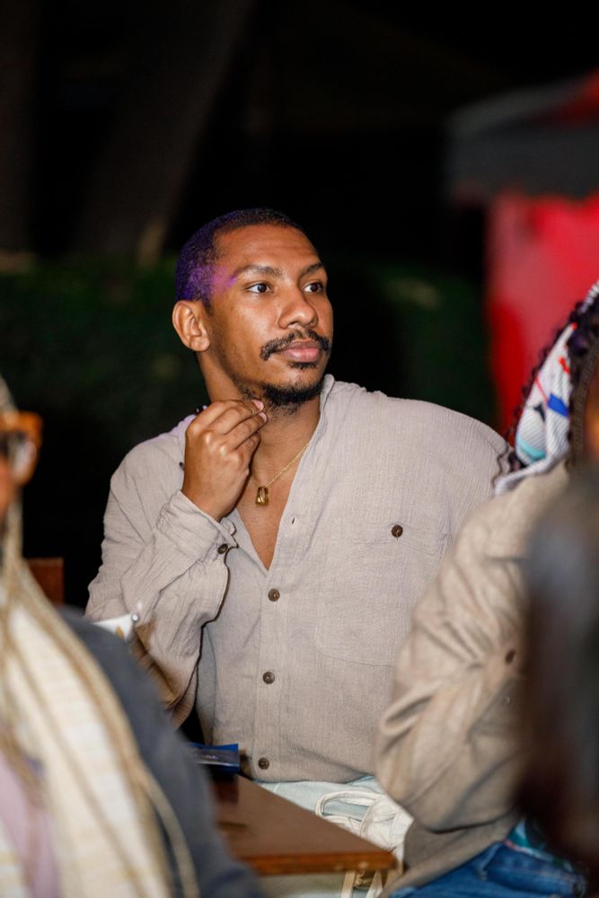 A picture of me in a greyish brown shirt looking to the side. Im a black person with short hair and a mustache. I have a gold chain holding a ring in it. 