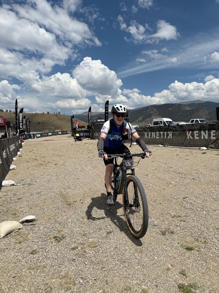 Rider on mountain bike coming in thru the finishing chute at Leadville Stage Race. Blue sky with fluffy white clouds in the background.