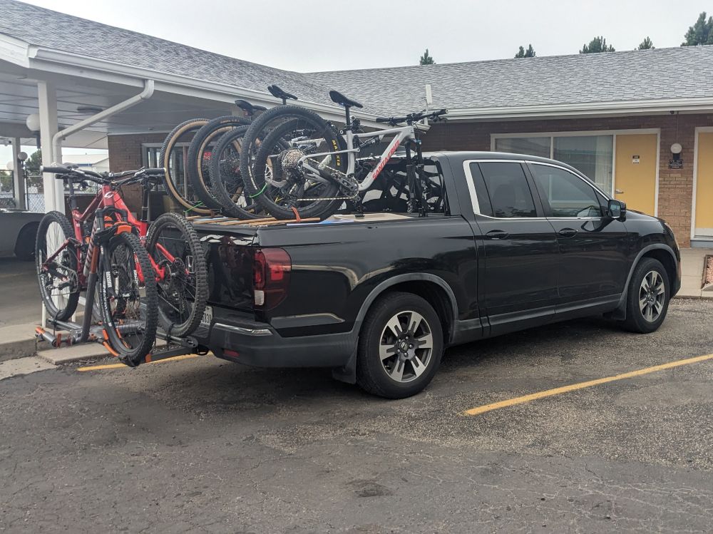 Black Honda Ridgeline pickup  loaded with 5 mountain bikes, 3 over the bed and 2 in a rear rack.