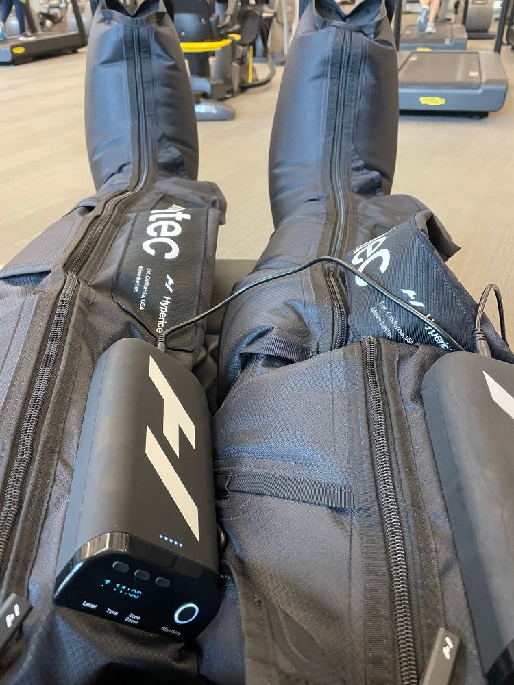 A pair of legs attached to a person in a recliner, and the legs are encased in Normatec inflatable leg thingies. 