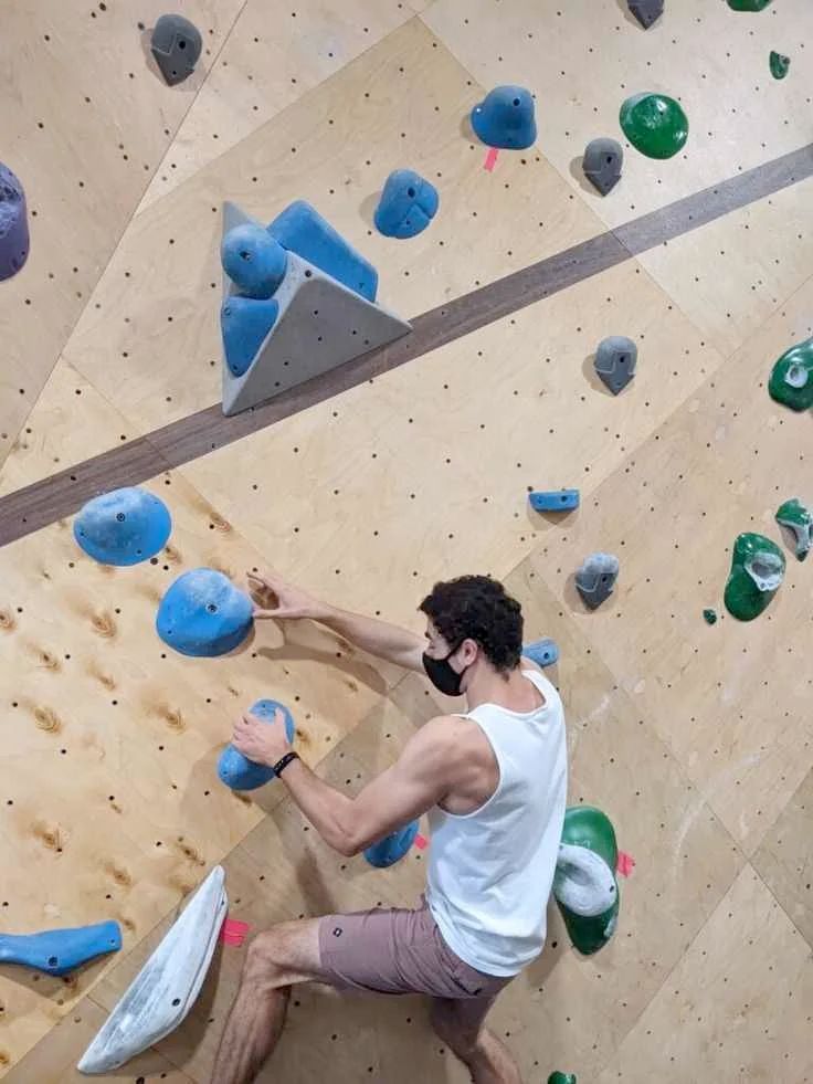 Luigi Mangioni bouldering off some juggy holds with a black face mask on
