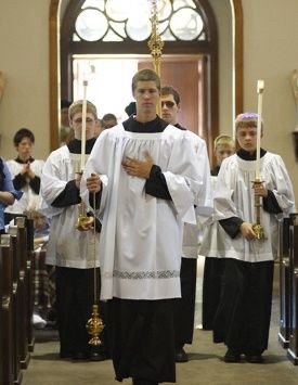 Protestant acolytes walking up the aisle of a church carrying candles in white robes. 