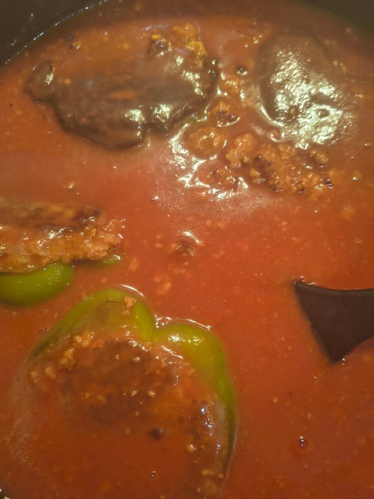 Die gefüllten Paprikahälften schwimmen im Topf, aufgegossen mit 1L Tomatensaft