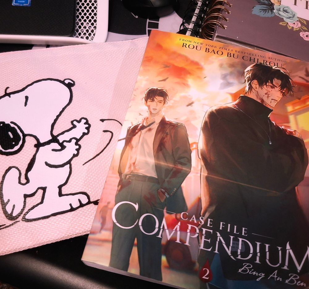 Photo of a snoopy pencil bag and Volume 2 of Case File Compendium: Bing An Ben by meatbun.