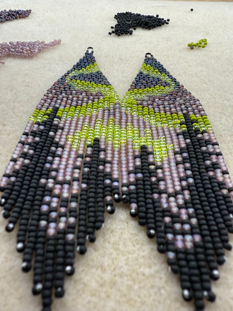 Fringe earrings made of iridescent beads depicting the northern lights over the shadows of old growth forest. 