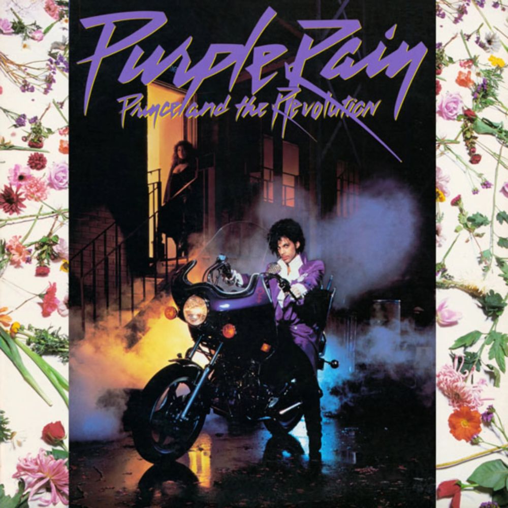 Cover of "Purple Rain" by Prince and the Revolution. Prince is sat on a massive motorbike on a stylishly gritty looking city street, dry ice billowing. A lady is waiting for him in a nearby doorway. There's a floral pattern on the left and right borders.