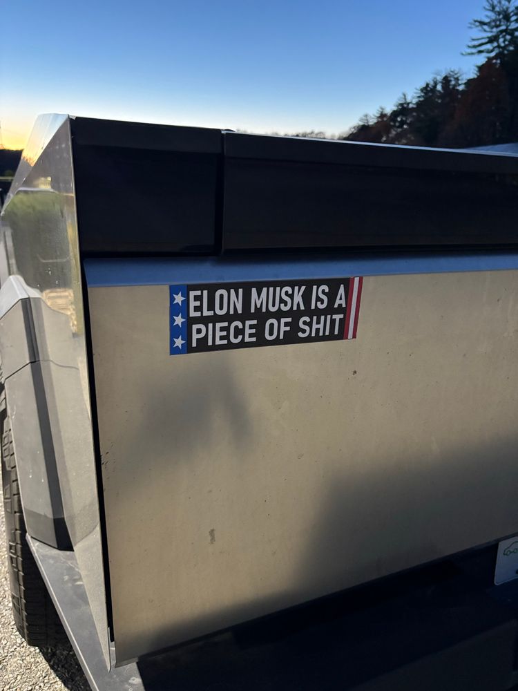Photo of the back of a Cyber Truck with a bumper sticker that reads, “ELON MUSK IS A PEOCE OF SHIT.”