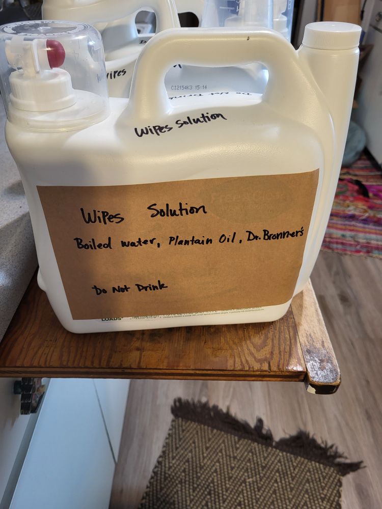 Picture of large liquid soap container with hand written wipes solution label on it that reads: wipes solution: boiled water, plantain oil, Dr. Brothers. Do not drink.