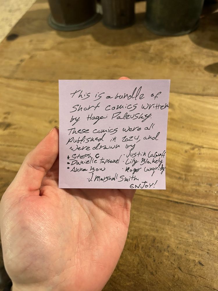 My hand, holding up post-it note that reads:

"This is a bundle of short comics written by Hagai Palevsky. These comics were all published in 2024, and were drawn by
Steph C
Danielle Taphanel
Anna Bow
Justin LaGuff
Lily Blakely
Roger Langridge
J. Marshall Smith

Enjoy!"