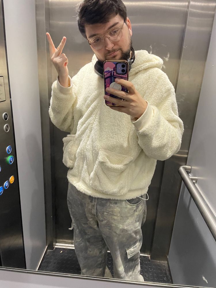 Me wearing a cream fluffy hoody and jeans taking a mirror selfie in an elevator