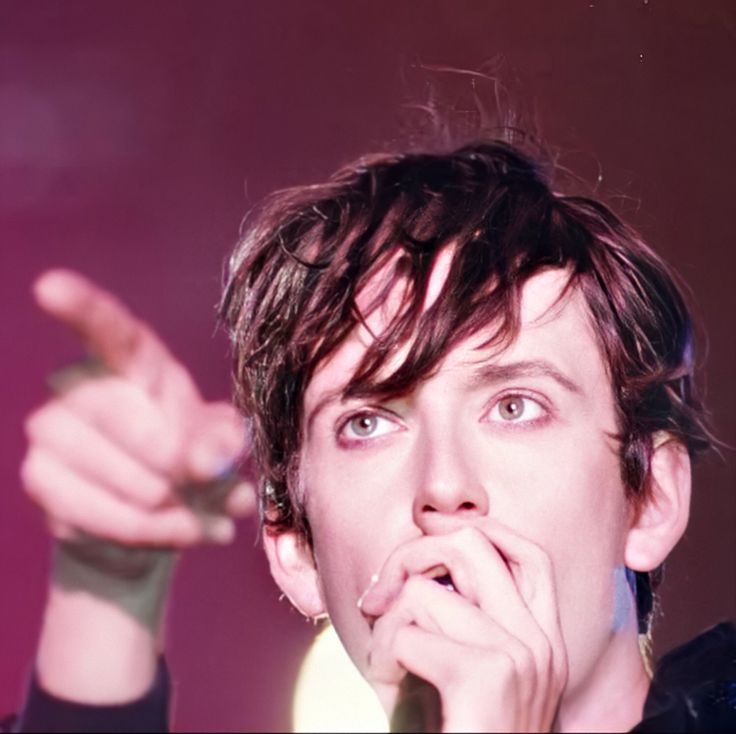 Picture of a younger Jarvis Cocker pointing and singing into a microphone held close to his mouth.
