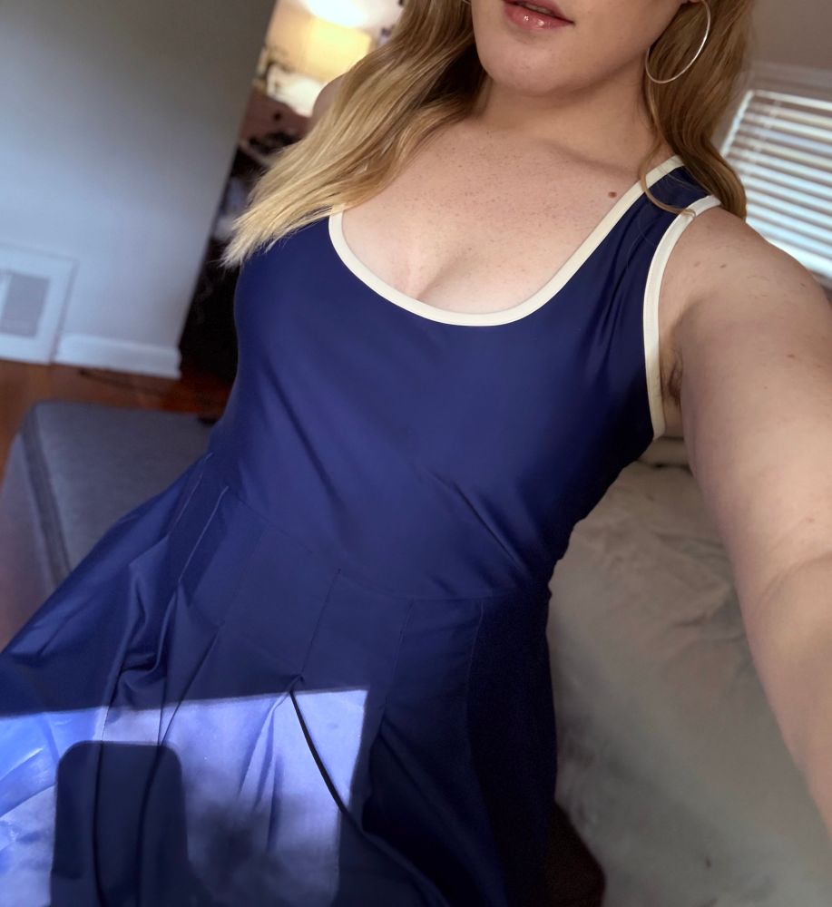 me wearing a navy blue tennis outfit. my long blonde hair is flowing over my shoulder, and i’m wearing red lip gloss and silver hoop earrings