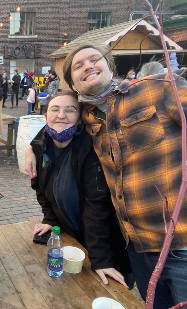 Sarah and Robin standing together smiling for the camera, Robin has his arm around Sarah