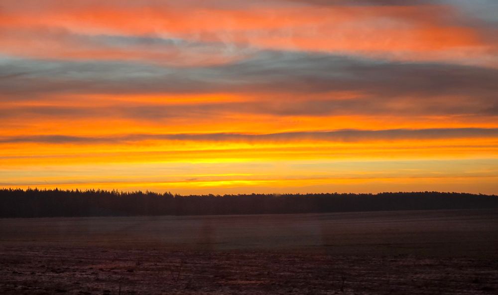 Sonnenaufgang mit Acker im Vordergrund. 