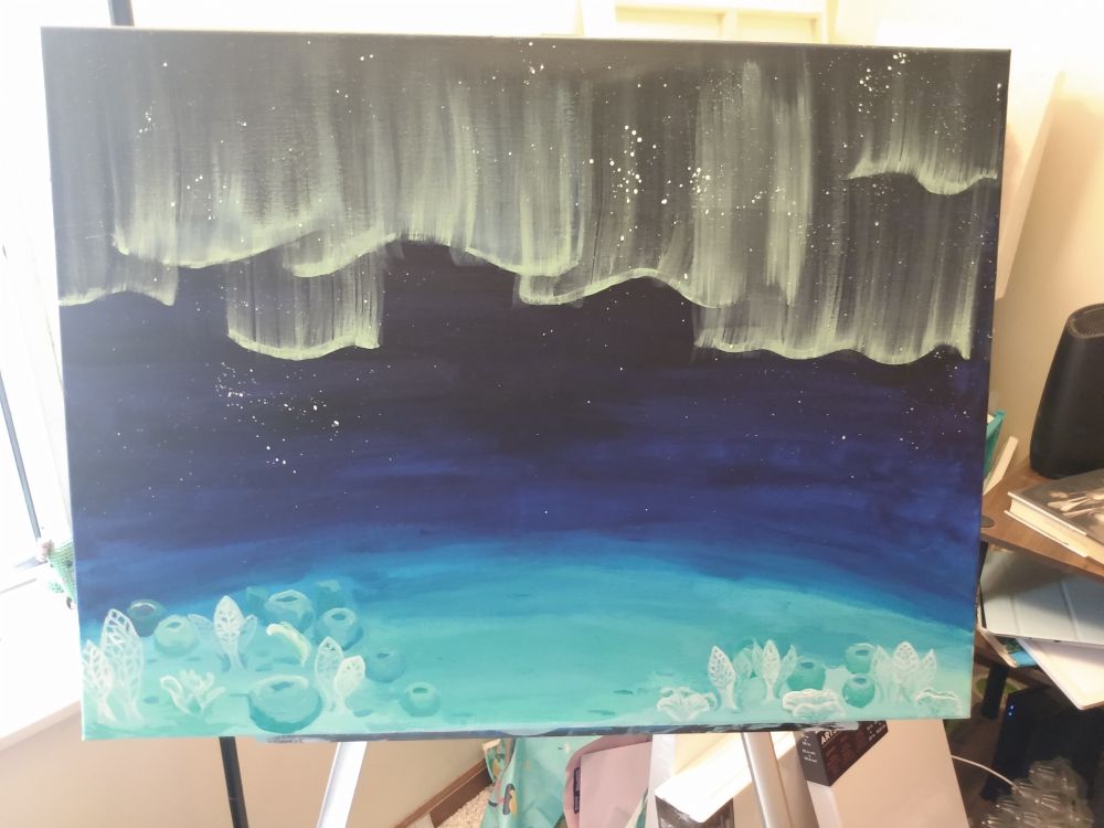 Photo of a large rectangular canvas with a partially completed painting. The base of the background is a gradient going from pale blue-green at the bottom through blue and indigo to black at the top. There are tiny white dots like stars on the darker part of the painting, along with some pale yellowish green veil-like ripples. At the bottom in front are sponges and corals like would be on the seafloor.