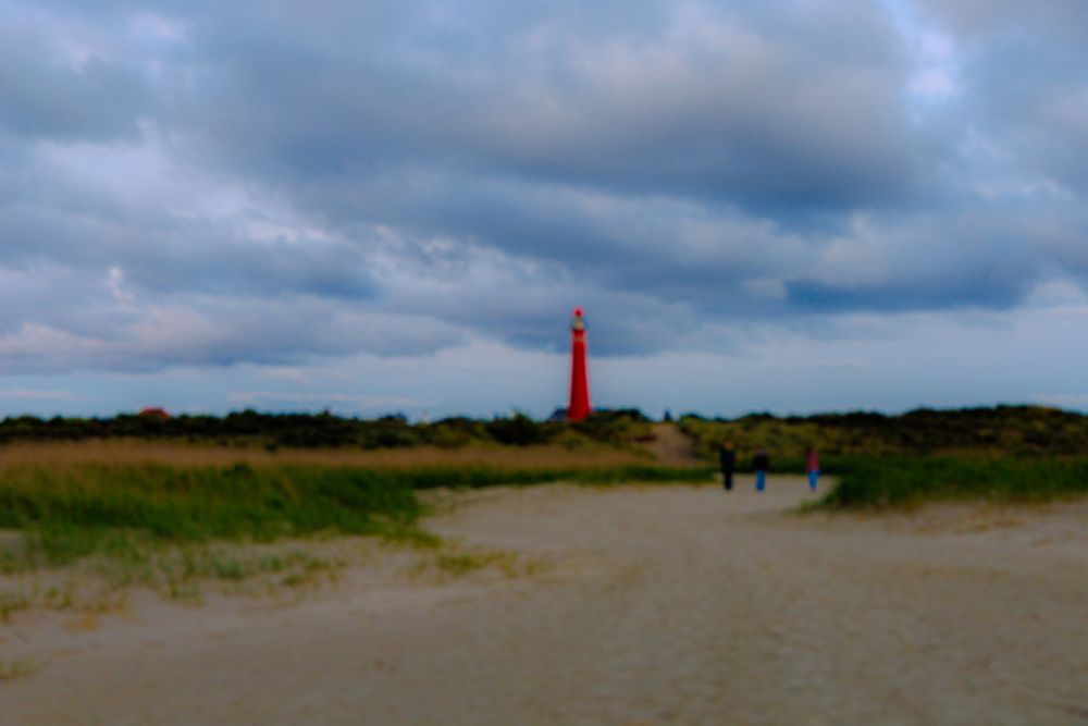 unscharfes Foto Blick vom Strand über die Dünen auf einen roten Leuchtturm.