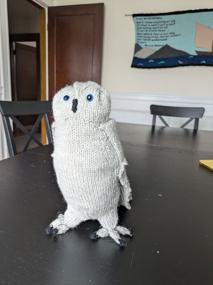 Front view of grey handknit owl sitting on a black dining table