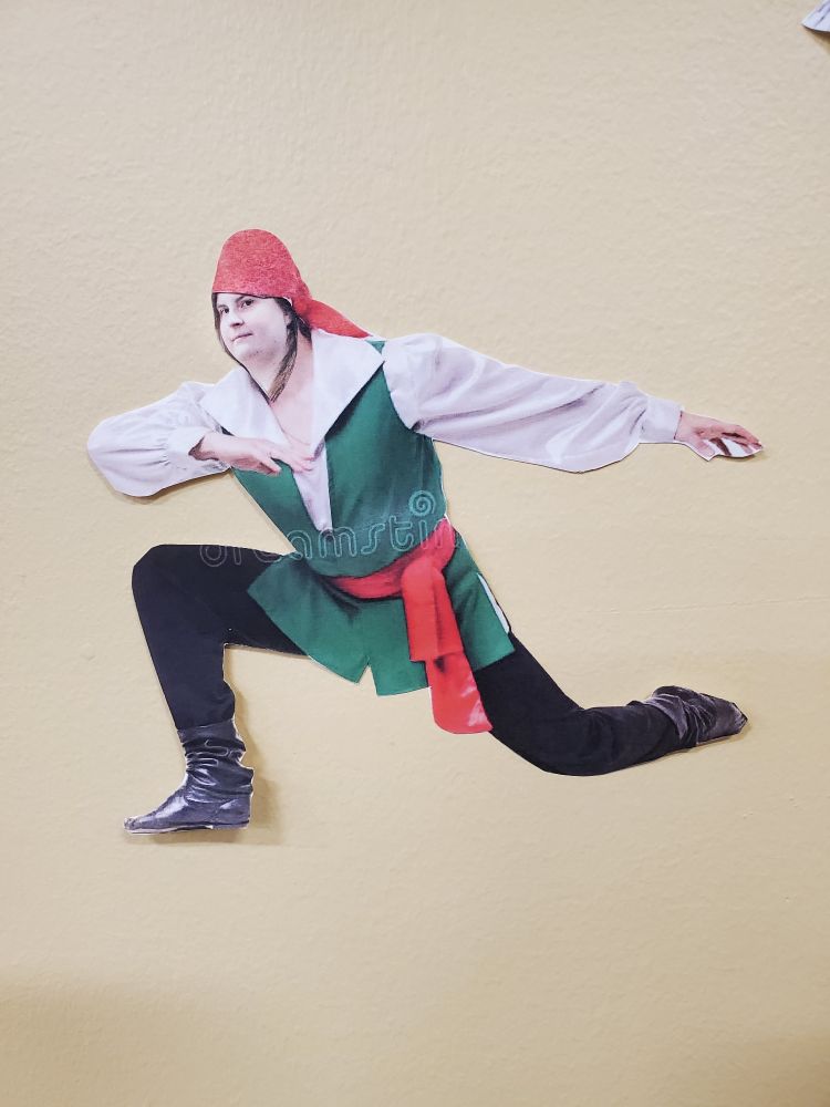 A pirate with Writer's face placed on top of the printed paper. The pirate is wearing black sagging boots and black pants. With a long sleeve, white undershirt and green vest, and a red cloth wrapped around the waist. A bandana wraps around the head.
The pirate is kneeling forward, with the hind leg nearly stretched out. The torso also leaning forward, with one arm leveled with the head and elbow bend inside to the head. And the other arm is lifted straight behind the body. 
The pirate oddly resembles a modern person in a "dab" position.