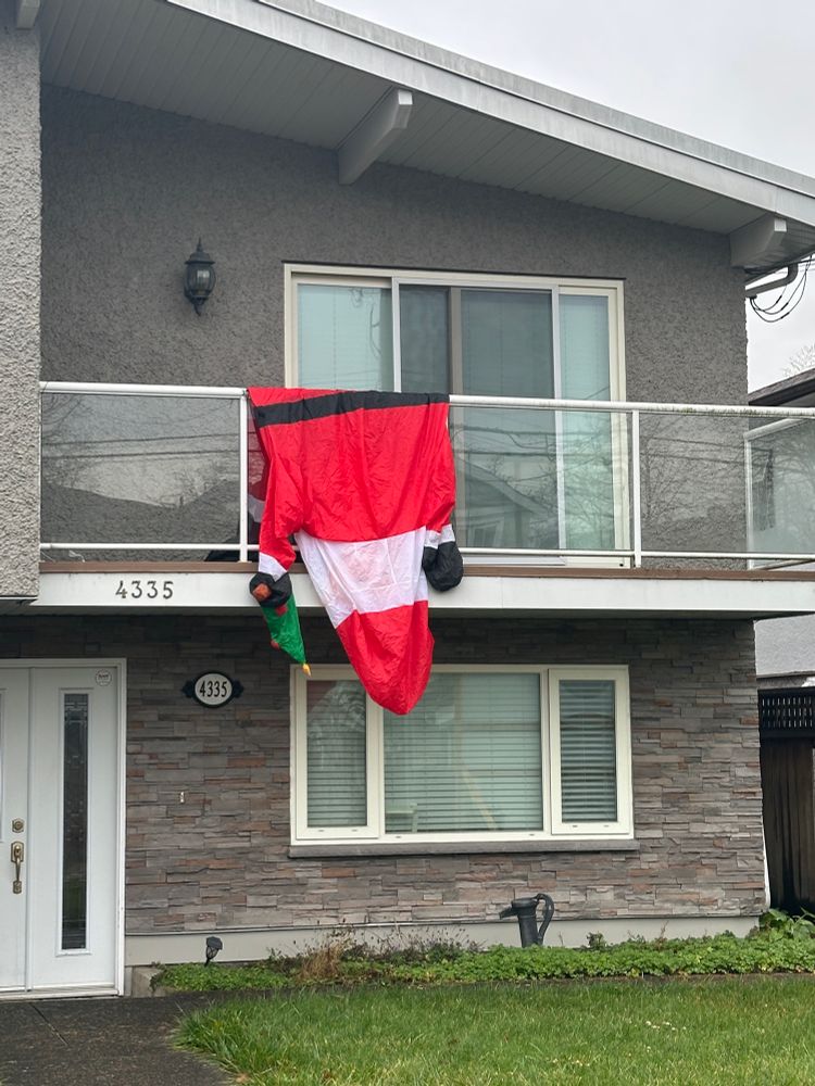 A deflated Santa inflatable decoration slumped over a patio railing on a house