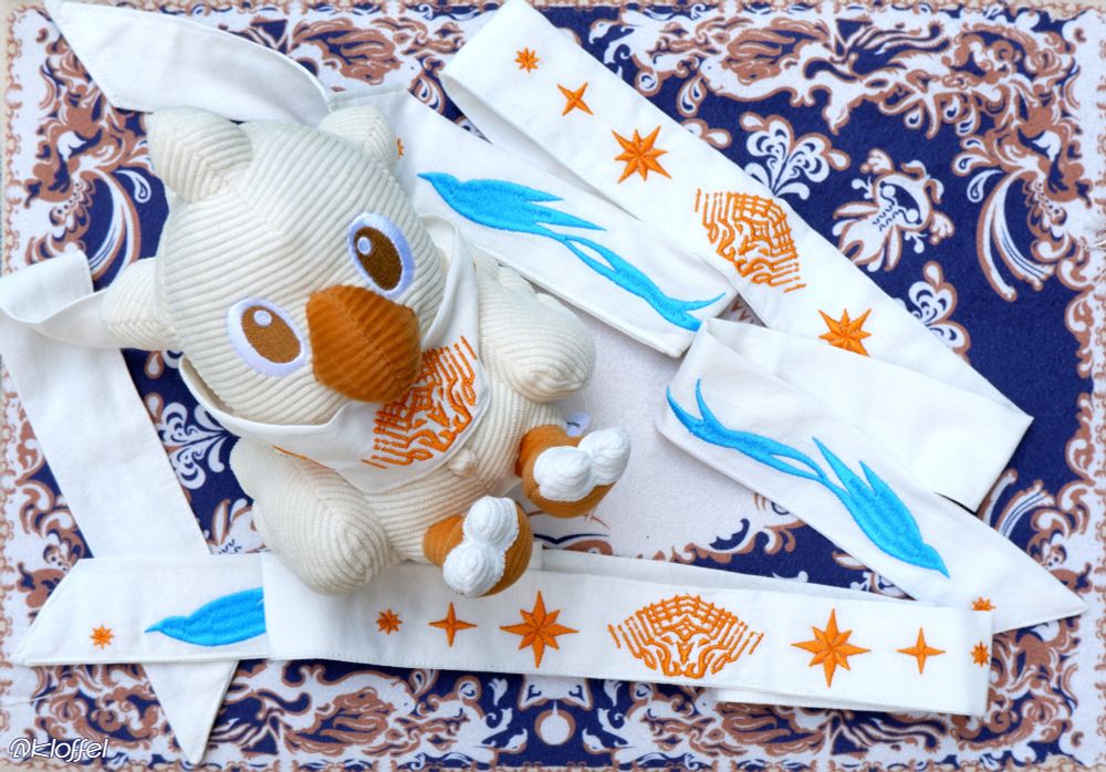 Linen ribbon with embroidered FFXIV Azem and Starbird designs, also with a Chocobo plush showcasing one of the ways to use the ribbon.