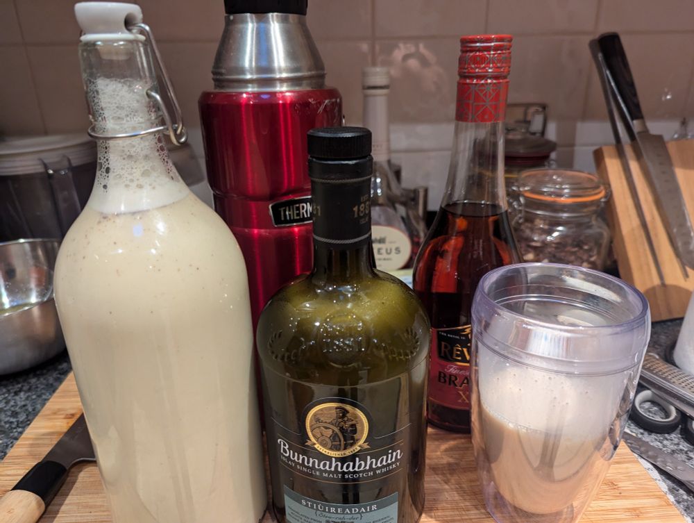 3 bottles of eggnog and a glass of eggnog mixed with brandy on a kitchen counter