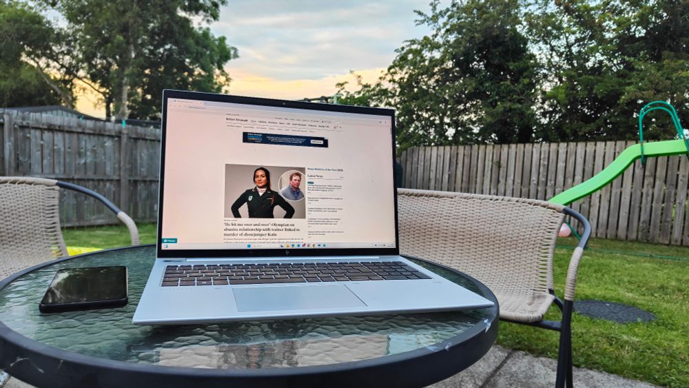 Laptop in the garden at dusk. Belfast Telegraph website on screen and phone to the left of laptop on a glass outdoor table.