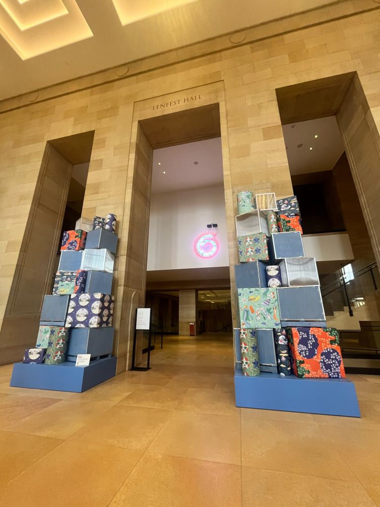 Two large piles of gifts at the entrance of the Philadelphia Museum with wrapping paper designed by Heritage Month collaborators, including Cindy Lozito